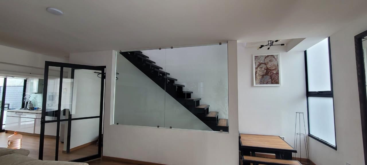 Puerta de marco negro y cristal junto a escalera con barandal de cristal